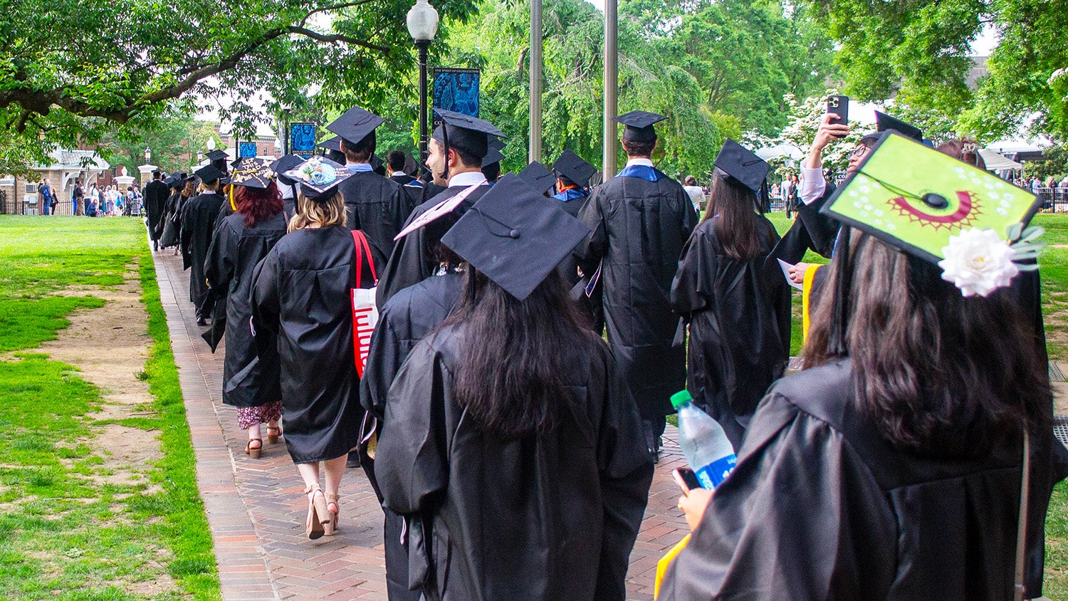 Graduating students process across Copley Lawn at Commencement, wearing their caps and gowns.